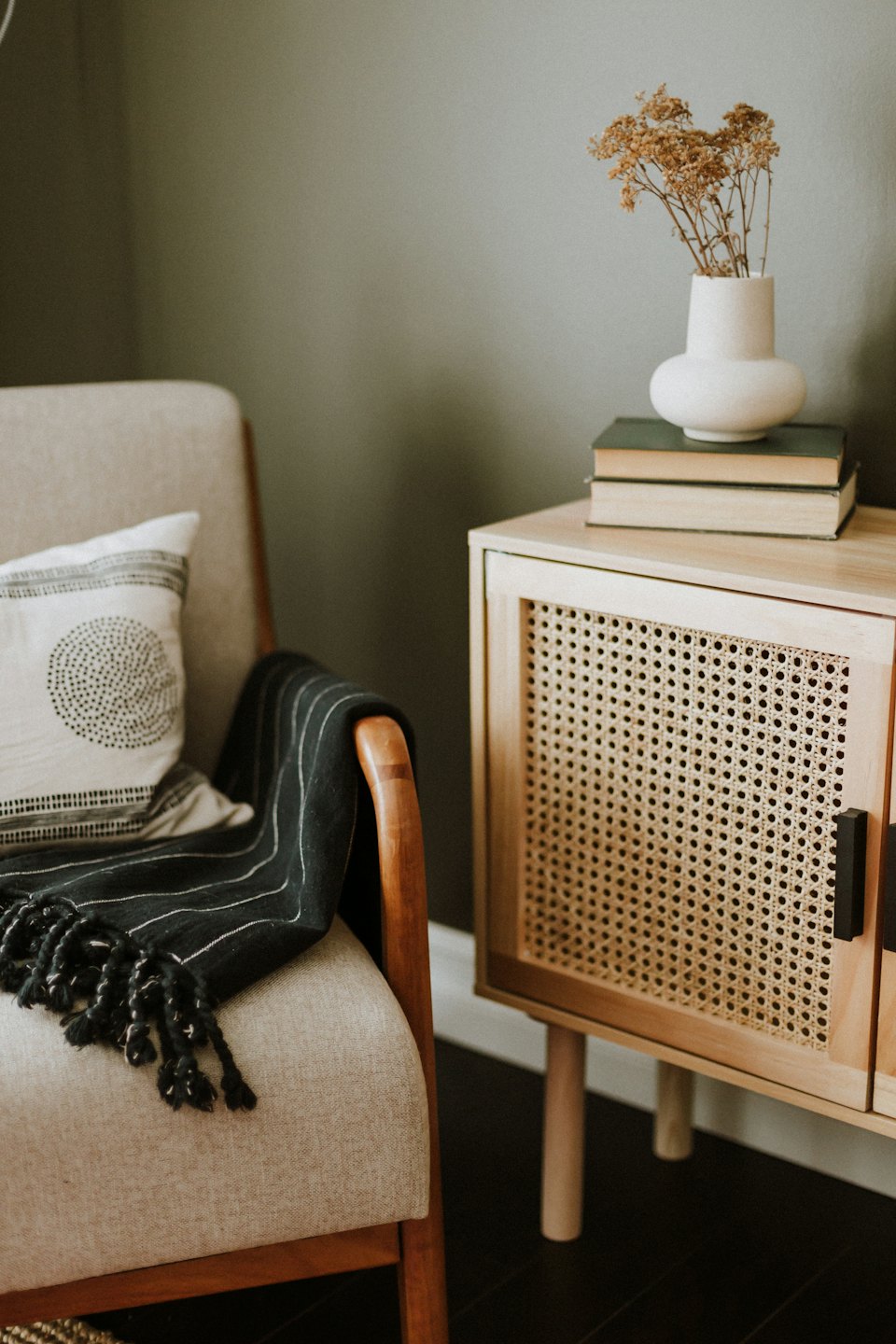 Modern armchair with throw blanket next to a cabinet with books.