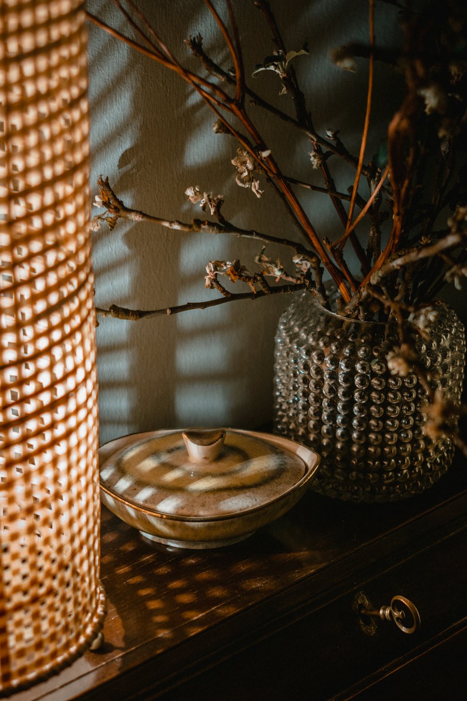 Woven lamp, ceramic dish, and glass vase on a wooden table.